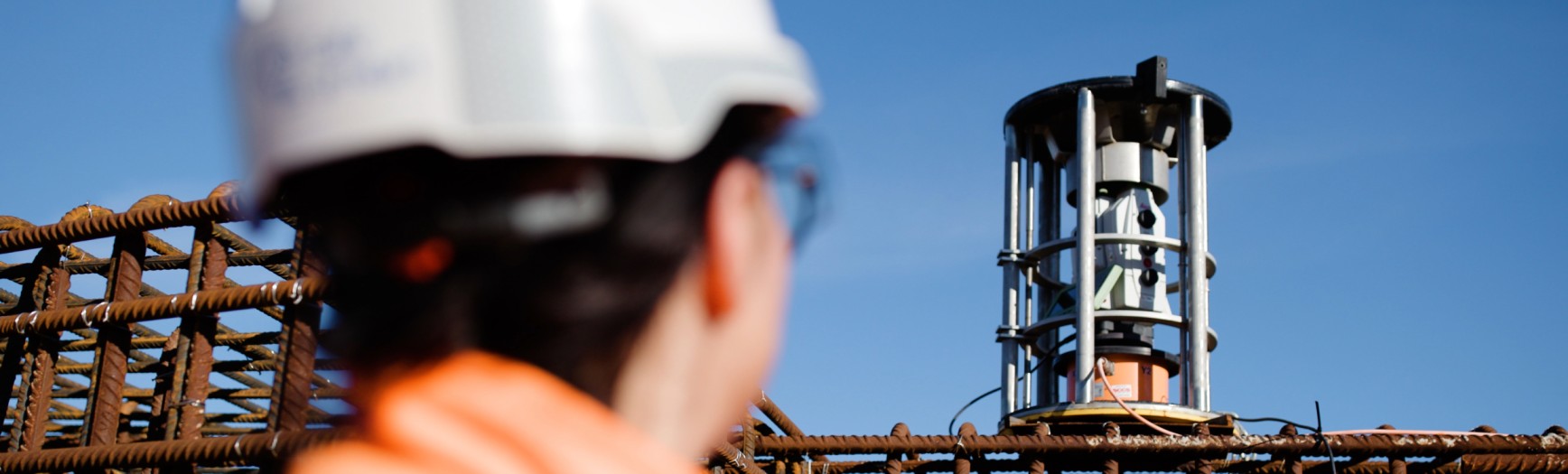 Construction worker in safety gear monitoring rebar structure with a monitoring total station on an active job site – construction safety, site monitoring, structural surveying technology